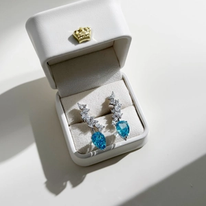 Macro shot of silver drop earrings with blue heart zircon in a white velvet jewelry box