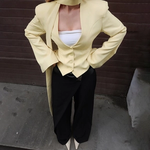 Detail of light yellow blazer with decorative buttons and ribbons and black trousers