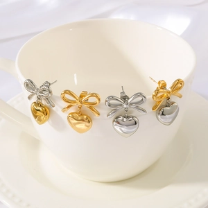 Bowknot heart earrings in gold and silver finishes on a white ceramic cup edge