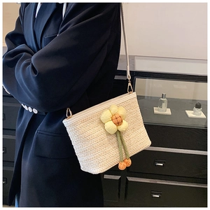 Close-up of woven straw crossbody bucket bag with decorative yellow knit flower detail