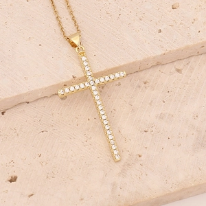 Detailed view of a gold-plated cross necklace with sparkling crystals on a stone surface