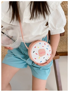 Pink donut-shaped crossbody bag with Hello print worn by child in natural setting