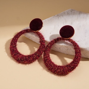 Detail of burgundy flocked hoop earrings with gold threading on a white stone background