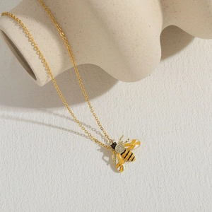 Macro view of golden bee pendant with enamel details and zircon on cross chain