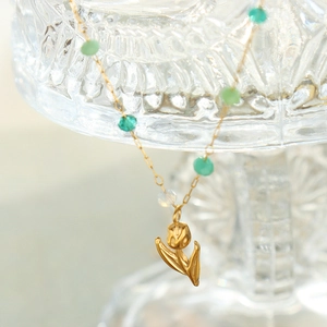 Elegant gold tulip pendant necklace with green crystal beads on a glass container
