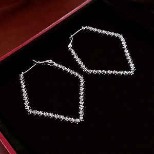 Detail of silver rhombus hoop earrings with textured finish in a red gift box