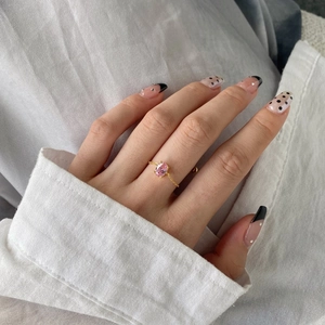 Close-up of a gold chain ring with a pink oval gemstone worn on a hand model
