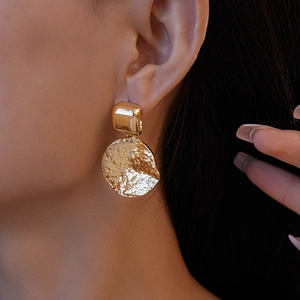 Gros plan de boucles d'oreilles géométriques dorées avec pendentif texturé sur l'oreille