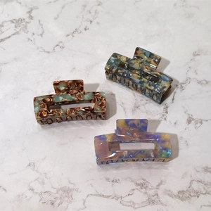 Flat lay of three rectangular acetate hair claws with marble textures on white stone