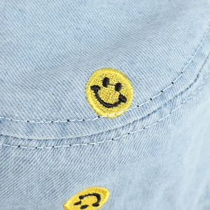 Close-up of yellow smiley face embroidery on blue denim fabric texture of a bucket hat