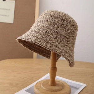 Detail of beige knit bucket hat texture on wooden stand in cozy indoor setting