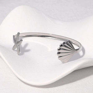 Silver starfish and scallop bangle displayed on a decorative white ceramic tray