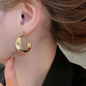 Close-up of polished gold C-shaped hoop earring on a model with a modern design