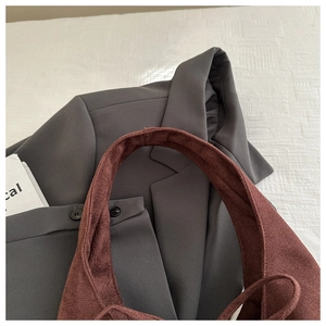 Detail of reddish-brown suede tote bag against a grey suit jacket background