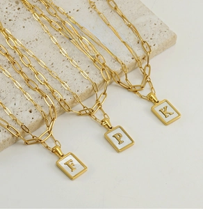 Close-up of 18K gold paperclip chain necklaces with square shell letter pendants on stone