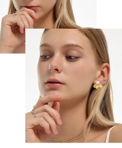 Close-up of golden pearl flower earrings paired with layered necklaces and a twist ring