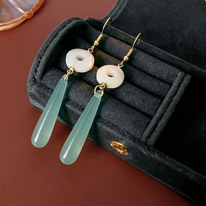 Detail of green resin teardrop earrings with white circular accents on black velvet