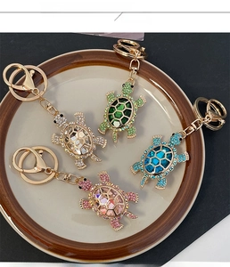 Colorful rhinestone turtle keychains in four colors displayed on a white ceramic plate
