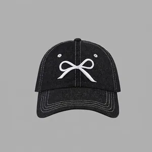 Detail of white bow embroidery and contrast stitching on a black denim baseball cap