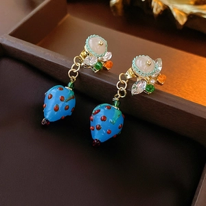 Macro shot of blue strawberry earrings with crystal beads and gold hooks on wood