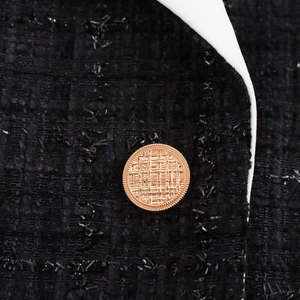 Gros plan du blazer en tweed noir avec bouton doré gaufré et détails de liseré blanc