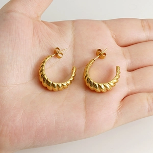 Golden spiral hoop earrings with croissant texture shown in hand with metallic gloss