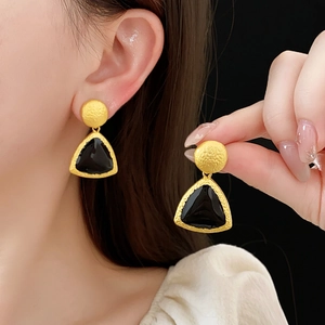 Close-up of vintage geometric gold matte earrings with black triangle enamel pendant