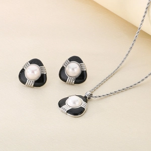 Dettaglio della collana a catena intrecciata e orecchini a triangolo con perla su beige