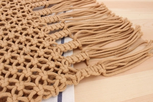 Close-up of handmade woven mesh pattern and long tassels on a khaki beach shoulder bag