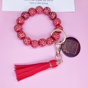 Détail de perles léopard rouges, frange en similicuir et charme en bois gravé MAMA