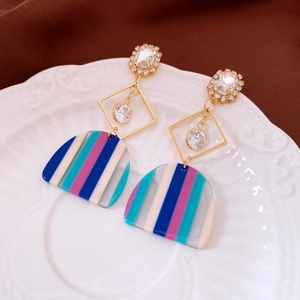 Detail of square zircon tassel earrings with striped colorful resin pendants on a ceramic plate
