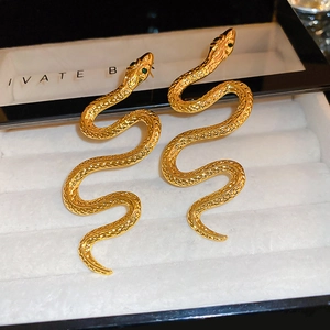Macro shot of gold snake-shaped earrings with green zircon eyes and scale texture
