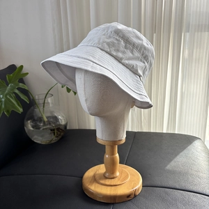 Detail view of a white lightweight sun hat with a side metal logo on a display stand