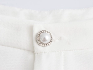 Detailed close-up of a decorative pearl button with silver trim on white twill trousers
