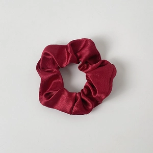 Close-up of a wine red satin scrunchie with silky luster and elastic pleated texture