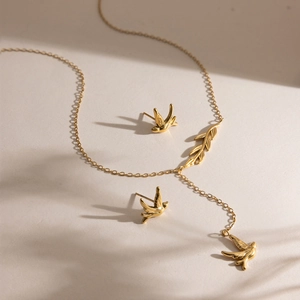 Gold-plated 18K stainless steel jewelry set with bird and leaf charms on textured base