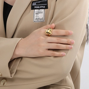 Close-up of polished 18K gold heart ring worn on index finger with elegant beige styling