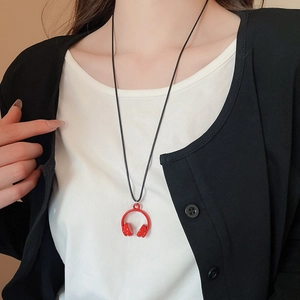 Close-up of a red headphone pendant necklace worn over a stylish white and black outfit