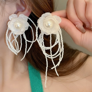 Detail of white lace flower earrings with pearl accents and long beaded tassels on model