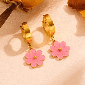 Macro shot of gold earrings with pink flower pendants on a textured warm background
