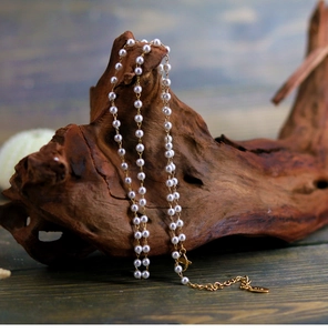 Detail of elegant white pearl necklace with 18K gold clasp on rustic wooden stand