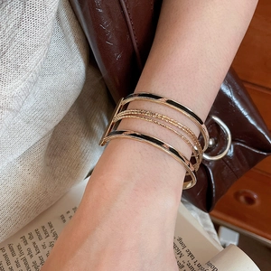 Detail of layered gold bracelet with black enamel drip and twisted wire texture
