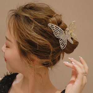 Elegant gold butterfly hair claw clip with rhinestones worn by a model on brown background