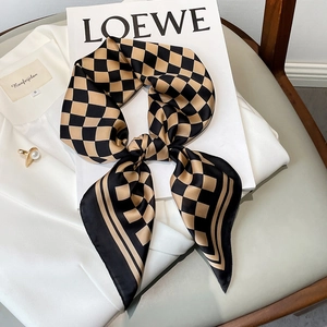 Fashionable black and gold checkered silk scarf tied in a bow on a white suit jacket