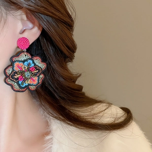 Close-up of embroidered floral earring featuring colorful threads and sparkling center crystal