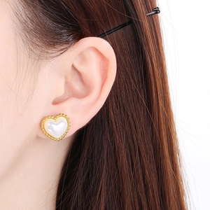 Close-up of gold heart stud earring with white shell inlay worn by a female model