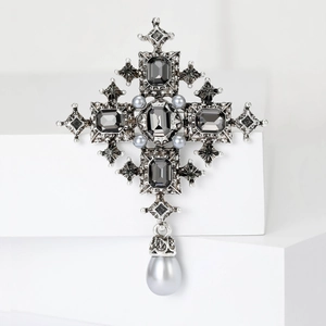 Baroque cross brooch with black gemstones and gray pearl pendant on a white stand