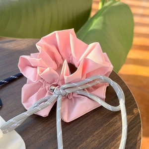 Detailed view of pink fabric drawstring bag with ruffled edges and thick grey rope on wood