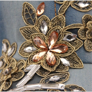 Detailed macro of gold floral embroidery and amber rhinestones on blue denim cap fabric