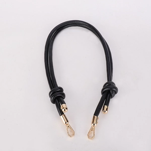 Detail of black leather bag strap with decorative knots and golden metal clasps